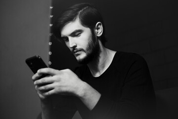 Portrait of young man typing on smartphone. Black and white photo.