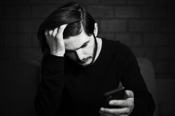 Close-up of sad man looking in smartphone. Black and white portrait.