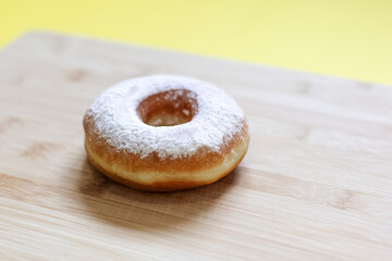 Close-up of donut sprinkled with white powder, on wooden table.