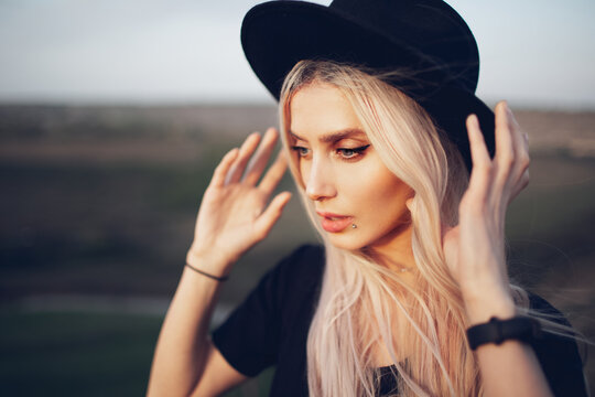 Portrait of pretty blonde girl wearing black hat outdoors.