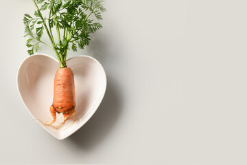 Freshly homegrown carrot unusual ugly shape in plate in shape of heart on gray background. Organic...