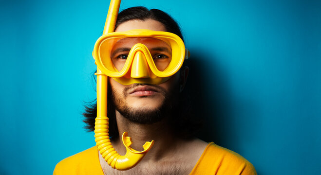 Young man in yellow, wearing diving mask and snorkel on blue background.