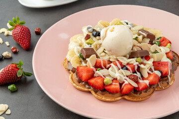 Heart waffle with banana and strawberry with gummy candy and ice cream on it.