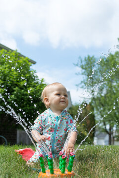 One Year Old (13 Months) Baby Playing In A Sprinkler In Their Front Yard; Water Play Wearing Sun Protective Swim Suit