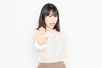 白背景の前に立って、NGのジェスチャーをする、レースのブラウスを着た若い女性