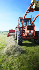 Old tractor with hay baler pressing summer hay.