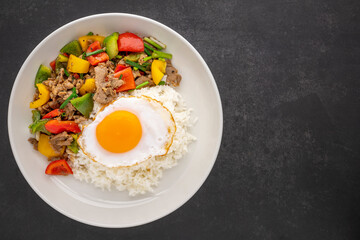 streamed rice topped with stir fried beef with black pepper, red, yellow, green sweet pepper, bell pepper or capsicum, spring onion and egg in ceramic plate on dark tone texture background, top view