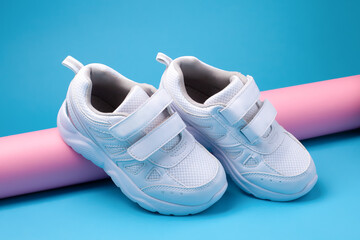 close-up of two white kid sneakers with Velcro fasteners for footwear on a pink, long paper roll on a blue background with soft light.
