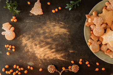 Christmas background with copy space: overhead of chalk board with homemade cookies sprinkled with icing sugar, sea buckthorn, golden pinecone, evergreen, golden dust, glitter