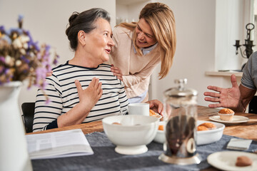 Woman sitting at the table and talking with friendly nurse in the retirement home