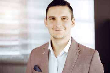 Friendly adult businessman in grey jacket. Business headshot or portrait in sunny office