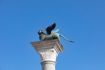 Bronze lion on the Piazza San Marco on blue sky background, Venice, Italy. Winged lion is a symbol of Venice. Ancient statue on a pillar close-up in Venice center