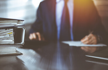 Binders with papers are waiting to be processed by unknown man accountant in blue blazer staying at home during covid pandemic. Taxes and audit concept