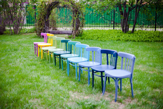 Diagonal Row Of Colorful Wooden Chairs On The Lawn In The Backyard, Preparing For A Micro Wedding Ceremony. 