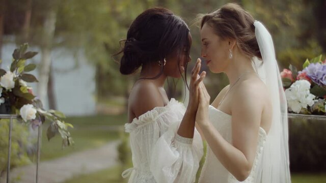 Wedding ceremony of a lesbian multi ethnic couple. Two young women in wedding dresses hold hands and kiss