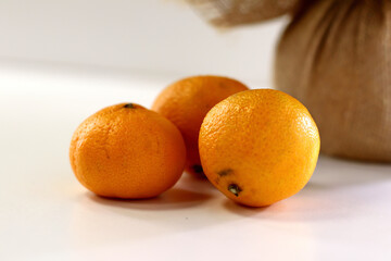 three tangerines on a white table and a brown bag behind