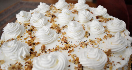 Close up shot of a beautiful White Egypt cake decorated with white roses and nuts crumbs