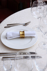 Festive table setting.White tablecloth with a textured pattern.Cotton napkin with a ring made of yellow metal.The concept of holidays.Wine glasses on the table. White plates.VIP-hall.Part of the