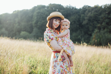 Portrait of pleasant smiling mom with little cute baby girl together on nature on summer day. Young...