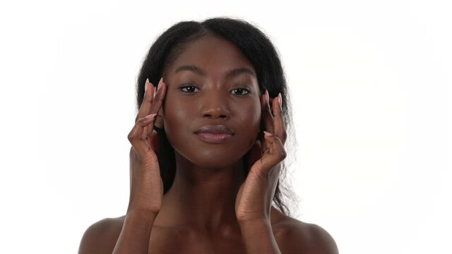 Portrait of a pretty African woman, running both hands along and down her face, looking at the camera. White background.