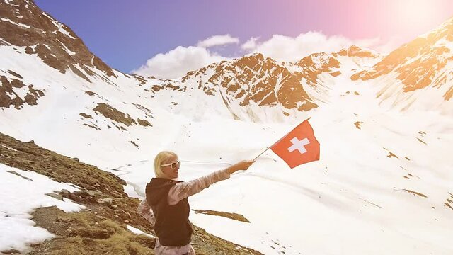 Tourist woman at with swiss flag in SLOW MOTION in the snow on top of Muottas Muragl mount of Switzerland. Popular mountain excursions in Graubunden canton of Switzerland.