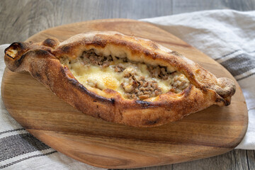 Peinirli with cheese and minced meat crispy baked and ready to serve. Greek open faced pizza on wooden cutting board placed above kitchen towel.