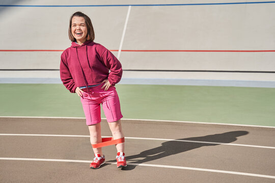 Dwarf woman laughing out loud while training at the sunny morning with elastic bands
