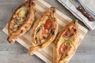 Peinirli with different flavours baked and ready to serve. Greek open faced pizzas on cutting board placed on wooden kitchen surface with towel and cutlery.