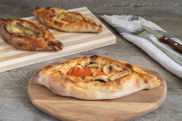 Peinirli with mixed flavours baked and ready to serve. Greek open faced pizzas on different cutting boards placed on kitchen surface with towel and cutlery.