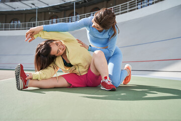 Woman helping to stretching to her midget friend or client while being at the stadium