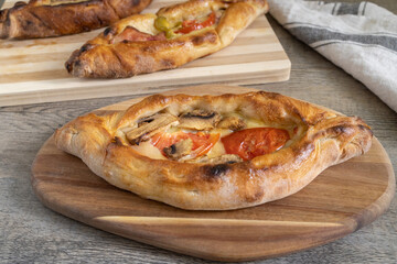 Peinirli with mixed flavours baked and ready to serve. Three Greek open faced pizzas on different cutting boards placed on kitchen surface with towel.