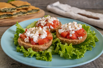 Burley rusks with chopped tomatoes and feta cheese served on lettuce leaves. Greek “Dakos” traditional food recipe accompanied with greens pie on wooden surface.