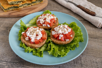 Burley rusks with chopped tomatoes and feta cheese served on lettuce leaves. Greek “Dakos” traditional food recipe accompanied with greens pie on cutting board.