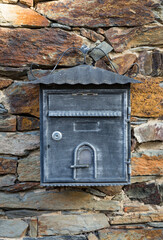 an antique gray and metallic mailbox hanging on a stone wall