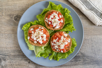 Burley rusks with chopped tomatoes and feta cheese served on lettuce leaves. Greek “Dakos” traditional food recipe. Wooden surface background with kitchen towel - top center view.