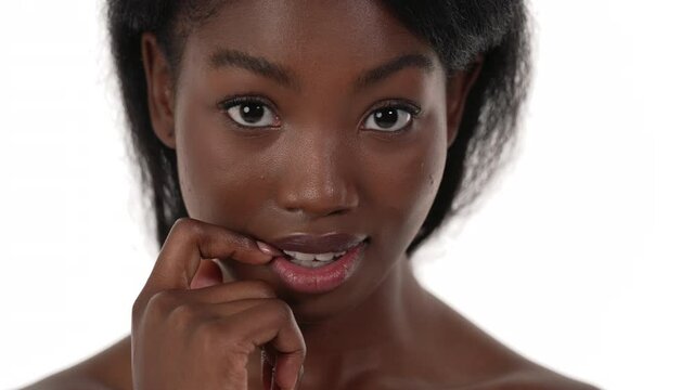 Close up of an african woman's face, looking down while biting her finger, timidly. White background.