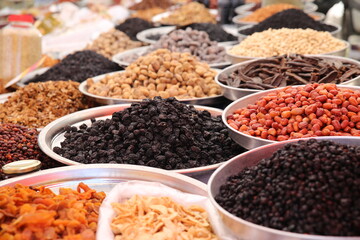Close up of a variety of dried raisins and sultanas on display in large metal trays in a bazaar.