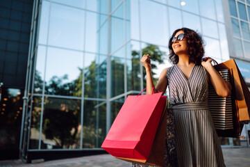 Cheerful woman enjoying shopping.  Fashion woman with shopping bags walking on street. Consumerism,...