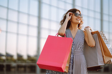 Cheerful woman enjoying shopping.  Fashion woman with shopping bags walking on street. Consumerism,...