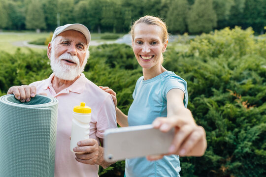 A blond sporty daughter take selfie photo with her father 80 year. Senior man very happy when go to walk and training at summer park, using smartphone . Concept care nurse with old people.