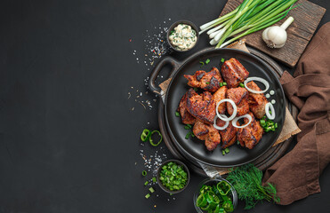 Pieces of fried meat with fresh onions on a black plate.