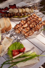 Composition of ready pork kebab, grilled vegetables. Green onions, cucumber and tomatoes on a white wooden background. Summer Picnic