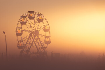 Big white Ferris wheel in a foggy park at dawn.