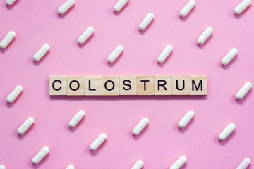 Word Colostrum. Wooden blocks with letters surrounded by pharmaceutical pills on pink background. Top view, layout