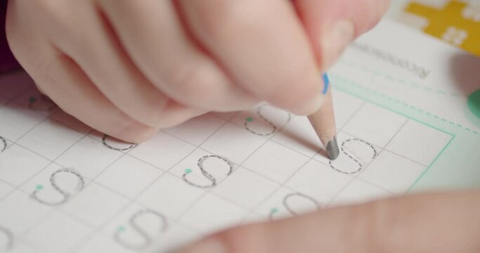 Close-up of a girl's hand learning alphabet writing the letter S on the school's book