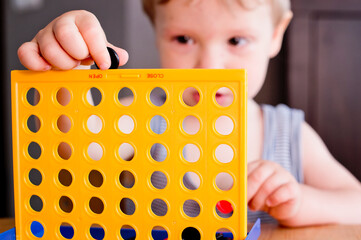 table game connect four. toodler playing game, by inserting checkers in to the grid. concentrated...
