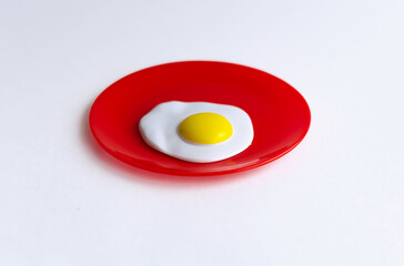 Plastic fried eggs in a red toy plate. The concept of "good morning". Breakfast time. It's time to wake up. Educational role-playing games for children. Kitchen utensils, household training.