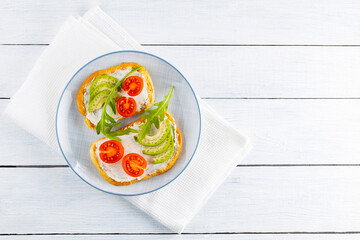 Avocado toasts with cream cheese and cherry tomatoes. Two toasts with avocado and arugula on white boards. Copy space. Top view