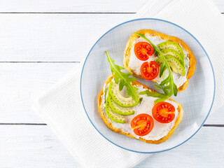 Avocado toasts with cream cheese and cherry tomatoes. Two toasts with avocado and arugula on white boards. Copy space. Top view
