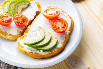 Avocado toasts with cream cheese on a white plate. Toasts with avocado and cherry tomatoes on a linen napkin. Healthy food. Close-up